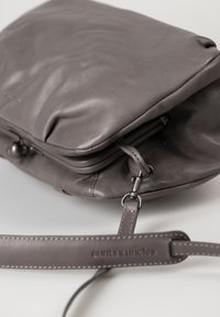 Borsa in pelle grigia con una superficie liscia, dotata di una lunga tracolla e dettagli di cucitura sottili. Due scomparti con bordi arrotondati.