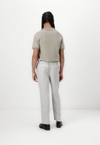 Camisa polo de malha cinza claro de mangas curtas, combinada com calças cinza claro ajustadas, apresentando um corte descontraído e cintura elástica. Inclui sapatos pretos.