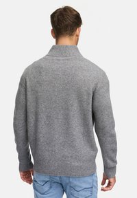 Grå stickad tröja med hög krage, ribbade ärmslut och nederkant. Tillverkad av mjukt tyg med en slät, texturerad yta.