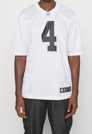 Uomo che indossa una maglia NFL bianca con il numero 4 in nero e pantaloni neri, in piedi davanti a uno sfondo bianco semplice.