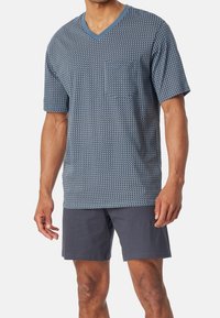 Korte mouwen, v-hals t-shirt in marineblauw met een geometrisch patroon en een zak, gedragen met donkerblauwe shorts. Glad stof en relaxte pasvorm.