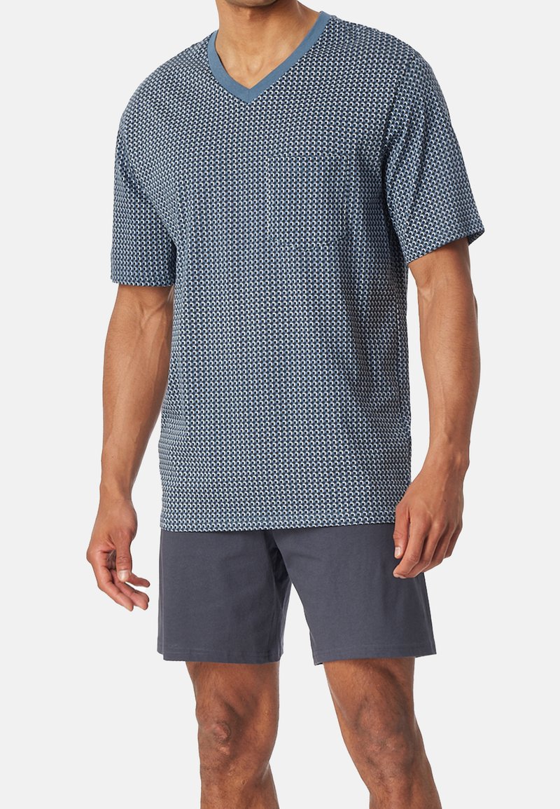 Korte mouwen, v-hals t-shirt in marineblauw met een geometrisch patroon en een zak, gedragen met donkerblauwe shorts. Glad stof en relaxte pasvorm.