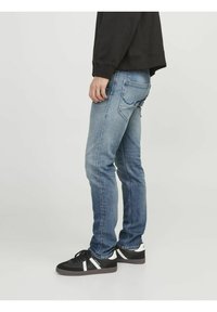 Jean en denim de couleur bleu clair avec une finition légèrement délavée, un design ajusté et des coutures visibles. Assortis à des baskets noires avec des accents blancs.