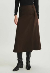 Jupe enroulée marron en tissu lisse, dotée d'une taille haute, de quatre boutons décoratifs sur un côté, et d'une silhouette évasée fluide.