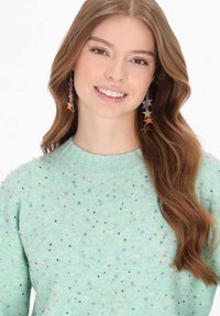 Mentazöld pulóver, különböző színű, texturált pöttyös mintával. A modellen színes csillag alakú fülbevalók láthatók, haja hullámos.