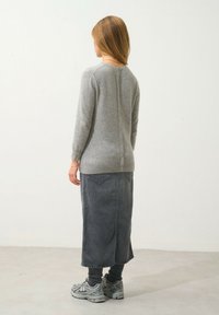 Maglione grigio in lana con chiusura a bottoni sul retro. Indossato con una lunga gonna di jeans scura e sneakers grigie con dettagli testurizzati.