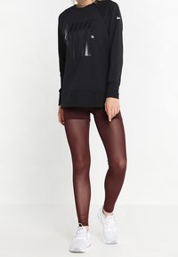 Sweat-shirt noir Nike avec un logo brillant, associé à des leggings bordeaux et des baskets blanches. Tissu lisse, design ajusté et longueur cheville.