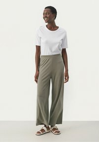 Chemise blanche à manches courtes, pantalon large vert olive et sandales blanches. Tissu lisse, coupe décontractée et taille ajustée.