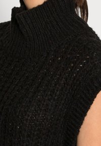 Czarny dziergany sweter z wysokim kołnierzem, prążkowaną fakturą i krótkimi rękawami z otwartymi bokami. Materiał ma miękki i gruby wygląd.