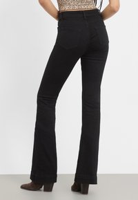 Sorte flared jeans med høy midje, laget av glatt denim. Har to baklommer og ferdig kant. Kombinert med brune hælhøye støvler.