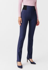 Marineblauwe high-waisted broek met zwarte tailleband; gladde stof; slim-fit ontwerp; voren met naaddetails; gecombineerd met blauwe suède hakken.