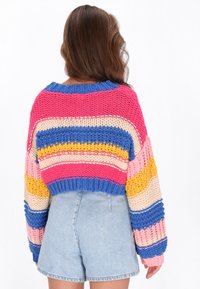 Nertinis megztinis pasižymi ryškiomis horizontaliomis juostelėmis rožinės, mėlynos, geltonos ir kreminės spalvų; laisvas siluetas su apvaliu iškirpimu ir didelėmis rankovėmis.