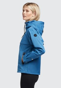 Blue waterproof jacket with a hood, side pockets, and adjustable drawstrings. Smooth, shiny texture. Features a circular logo on the sleeve.