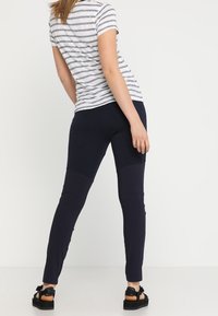 Leggings azul marino con paneles de textura contrastante. La modelo lleva un top de manga corta a rayas grises y blancas y sandalias negras.