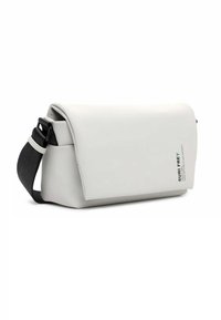 Bolso mensajero blanco hecho de un material liso y duradero. Cuenta con una solapa plegable, una correa negra ajustable y una etiqueta de texto verde en el lado.