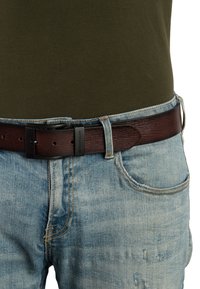 Bruine leren riem met een gestructureerde afwerking, voorzien van een matte zwarte metalen gesp. Draagt over vervaagde lichtblauwe spijkerbroek.