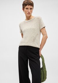 Κοντομάνικο πλεκτό μπλουζάκι σε ανοιχτό γκρι χρώμα με πολυχρωμές βούλες. Διαθέτει λεπτομέρειες από ανοιχτό ύφασμα και ραμμένο γιακά, συνδυασμένο με μαύρα παντελόνια και πράσινη τσάντα.