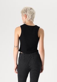 Μαύρο αμάνικο crop top με στρογγυλή λαιμόκοψη, κατασκευασμένο από λείο ύφασμα, συνδυασμένο με καφέ και λευκές ρίγες παντελόνι.