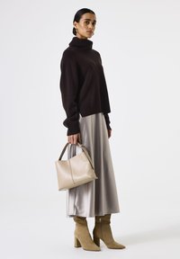 Suéter de cuello alto marrón oversized, falda de satén plateado, bolso beige y botines de gamuza marrón con tacón de bloque. Texturas suaves y diseño estructurado.