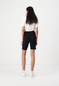 Black bermuda shorts, elastic waistband, smooth fabric, paired with a white short-sleeve shirt and white sneakers, viewed from the back.