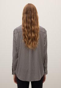 Chemise à manches longues à rayures noires et blanches avec une coupe décontractée et un ourlet arrondi, dotée de poignets boutonnés et d'une texture de tissu lisse.