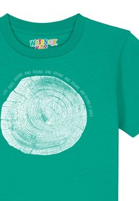 Teal katoenen t-shirt met een gedrukt boomringontwerp met concentrische cirkels en tekst: "Het leven draait rond en rond en rond het gaat."