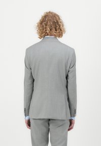 Light gray suit jacket with a smooth texture, single vent at the back, worn over matching trousers, showing a light blue shirt beneath.