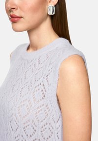 Helles lavendelfarbenes gestricktes ärmelloses Oberteil mit einem strukturierten Rautenmuster. Ein glattes silbernes quadratisches Ohrloch ergänzt das Design.