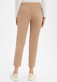Tan, slim-fit pants with a smooth texture, elastic waistband, and two back pockets. Styled with white sneakers.