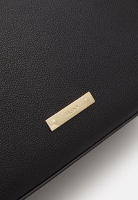 Czarna, teksturowana skóra z małą, prostokątną, złotą metalową tabliczką z wygrawerowanym napisem "ALDO".