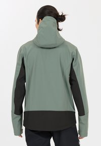 Hooded jakke i lys grøn med sorte detaljer. Har en glat tekstur, strømlinet form og en høj krave for beskyttelse.