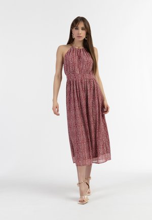 Rotes Neckholder-Kleid mit floralem Muster, tailliertem Schnitt, fließendem Rock und leichtem Stoff. Kombiniert mit klaren Sandalen mit Absatz.