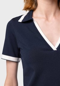 Mörkblå polo med V-ringning, med vita randiga detaljer på kragen och ärmarna, tillverkad av ett strukturerat tyg.