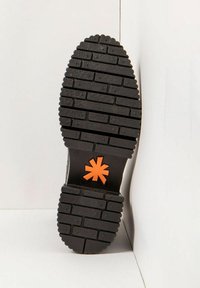 Semelle de chaussure noire avec un motif de chaussée en briques et un logo en forme d'astérisque orange près de l'arche, présenté sur un fond blanc en coin.
