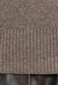 Braun gerippter Strickstoff überlappt mit strukturiertem dunkelbraunem Leder. 