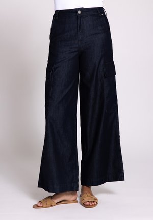 Wide-leg cargo pants in dark denim; features side pockets, a button at the waist, and a smooth texture. Stylish slip-on sandals complete the look.