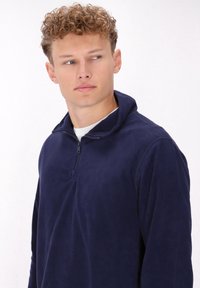Pullover in pile blu navy con colletto a zip, texture morbida e maniche lunghe. Caratterizzato da una vestibilità casual e rilassata e dettagli minimal.