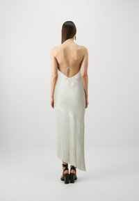 Satin midi haljina u svijetlo sivoj boji s niskim leđima, tankim trakama i resicama na jednoj strani. Uparena s debelim sandalama na visoku petu u crnoj boji.