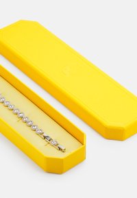 Rhinestone-Armband in Silber, präsentiert in einer gelben achteckigen Box mit strukturierter Oberfläche und goldenem Innenfutter.
