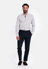 Geruite button-up shirt in wit en marineblauw met lange mouwen, gecombineerd met donker marineblauwe slim-fit broek en zwarte instapschoenen.