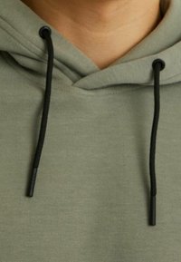 Felpa verde oliva con cappuccio regolabile, caratterizzata da un cordino nero con punte. Tessuto morbido con dettagli di cucitura minimi.