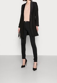 Svart dubbelknäppt blazer över en ljusrosa topp, ihop med smala svarta byxor med sidosträck, och svarta stilettklackar.