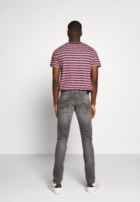 Camiseta a rayas burdeos y gris combinada con jeans grises ajustados, que cuentan con bolsillos traseros y costuras mínimas, llevada con zapatillas blancas.