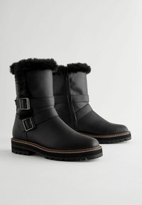 Bottines noires en cuir avec bordure en fausse fourrure, dotées de deux sangles ajustables avec boucles en métal et d'une semelle en caoutchouc texturé pour une meilleure adhérence.