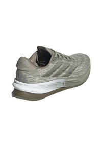 Zapatilla de running Adidas en gris claro, con tejido texturizado, tres rayas en el costado, una entresuela blanca y el texto "DREAMSTRIKE" en la suela exterior.