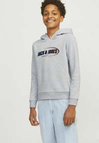 Felpa grigia con logo frontale "JACK & JONES." Presenta un cappuccio con cordino, polsini a coste e una vestibilità comoda, abbinata a jeans azzurri chiari.