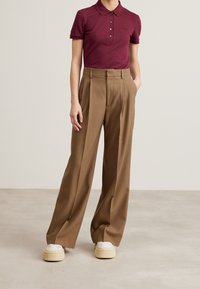 Polo shirt bordeaux avec patte de boutonnage, associé à un pantalon marron taille haute et à jambes larges. Les chaussures sont blanches avec une semelle épaisse et texturée.