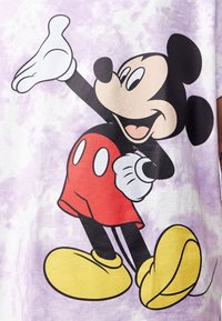 Fialové tričko s tygrováním ve stylu tie-dye s grafikou Mickey Mouse, černým a červeným designem, žlutými botami, bílými rukavicemi a výraznými rysy obličeje.