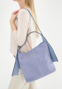 Blød lavendel læder tote taske med en glat overflade, kontrasterende blå håndtag og et rummeligt, åbent design. Ingen synligt hardware.
