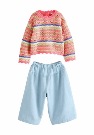 Mehrfarbiger Strickpullover mit Wellenkante, der rosa, gelbe und blaue Streifen aufweist, kombiniert mit hellblauen, locker sitzenden Shorts.